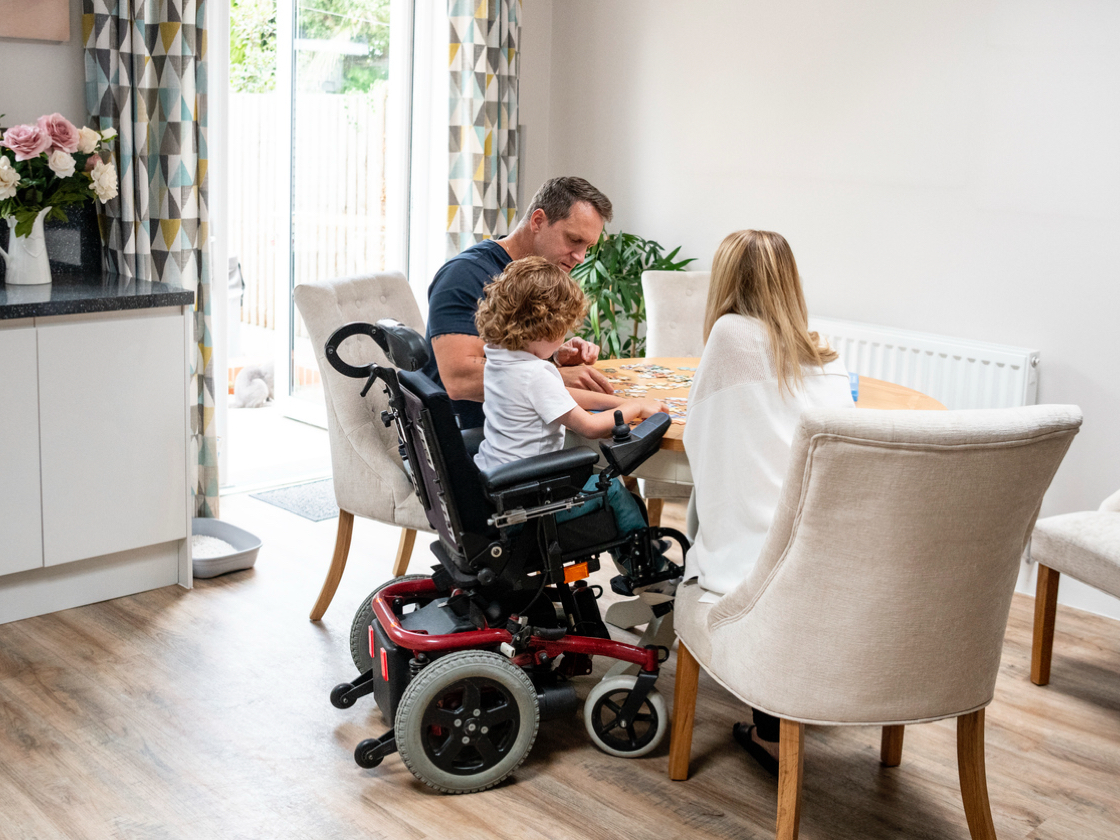 Family sitting together at home, including a child in a wheelchair, spending quality time around the table.